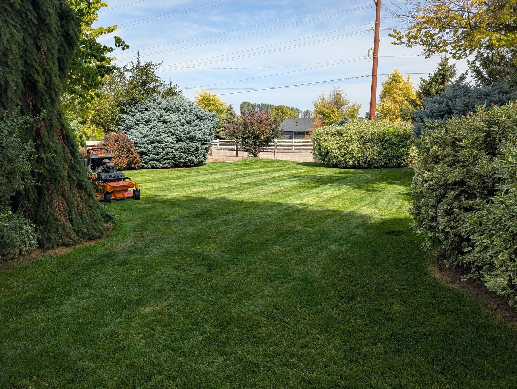 A professionally maintained green lawn with clean mowing lines and lawn equipment visible at the edge of the property